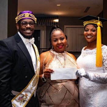 Three smiling adults in formal attire holding envelope