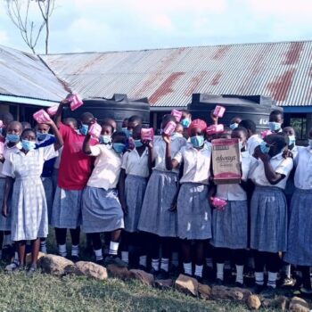 Students holding pink hygiene kits outside school